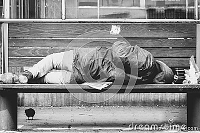 Poor homeless man or refugee sleeping on the wooden bench on the urban street in the city, social documentary concept, black and w Stock Photo