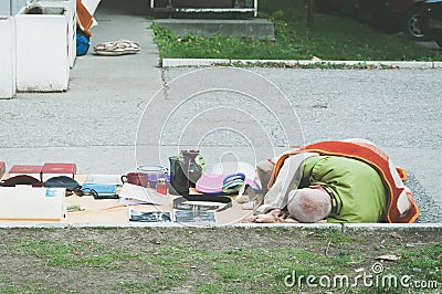 Poor homeless street vendor sleeps on the ground covered with blanket. Editorial Stock Photo