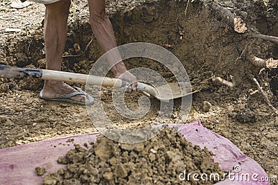 A poor man digging into the ground with a shovel, excavating a hole for a house foundation. Menial and unskilled job Stock Photo