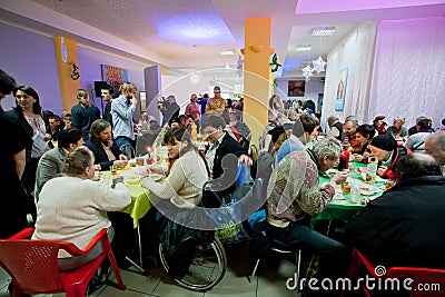 Poor people sit around tables with food at the Christmas charity dinner for the homeless Editorial Stock Photo