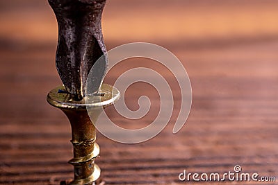 a poor-quality screw is screwed into a brown wood with a screwdriver Stock Photo