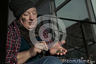 Poor senior man counting coins on stairs indoors Stock Photo