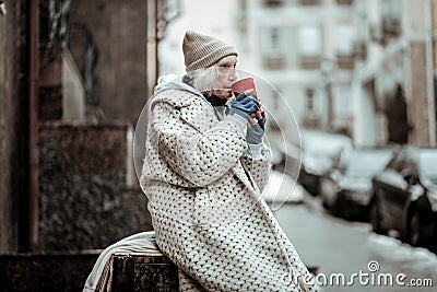 Poor senior woman drinking tea on the street Stock Photo