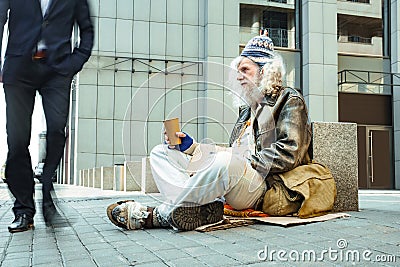 Poor starving man in tattered clothes sitting outside Stock Photo