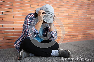 Poor tired stressed depressed elderly Asian woman homeless sitting on the street in the shadow of the building and begging for Stock Photo