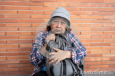 Poor tired stressed depressed elderly Asian woman homeless sitting on the street in the shadow of the building and begging for Stock Photo