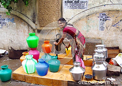 Poor young Indian woman in a sari with colorful pots near the water source Editorial Stock Photo