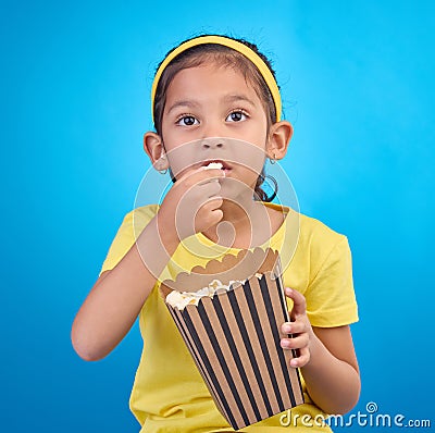 Popcorn, eating and focus with girl in studio for food, cinema and relax. Television, movie and film with child and Stock Photo