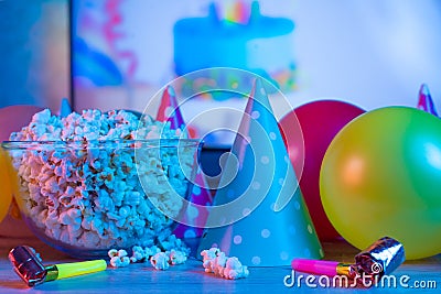 Popcorn with festive accessories on the background of TV. Watching TV on the occasion of a family celebration or in a circle of Stock Photo