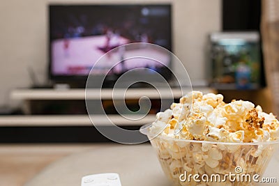 Popcorn and remote control on sofa with a TV broadcasting basketball match Stock Photo