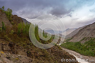 Poplar trees and small running river small lying in a rocky valley underlying blue cloudy sky Stock Photo