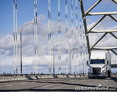 Popular big rig white long hauler semi truck transporting cargo in dry van semi trailer driving on the road on the truss arched Stock Photo