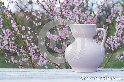 Porcelain pink jug on a table of white boards against the background of a flowering bush Stock Photo