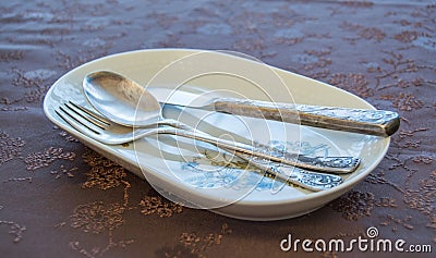 Porcelain plate with flower decorations, a silver knife, fork and a spoon on a decorated cover Stock Photo