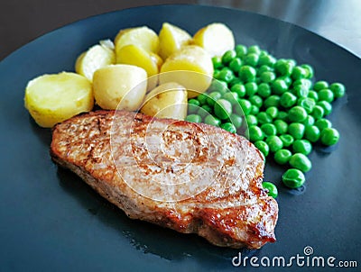 Pork chop with baby potatoes and peas. Selective focus. Stock Photo