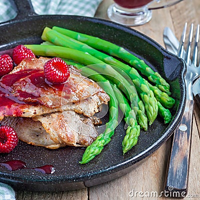 Pork cutlets with raspberry sauce and asparagus in iron cast pan, square Stock Photo