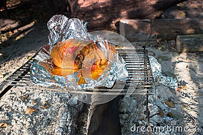 Pork leg meat in foil is heated on coals on a barbecue in nature. Background Stock Photo