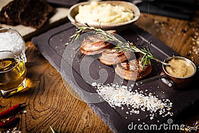 Pork tenderloin with mashed potatos, bacon and mustard sauce covered with a branch of smoking rosemary on black board Stock Photo