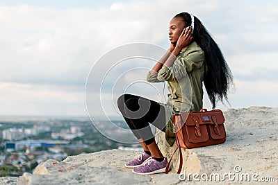 Porrtrait of gorgeous african american hipster woman with smartphone and headphones listening to music over blue cloudy Stock Photo