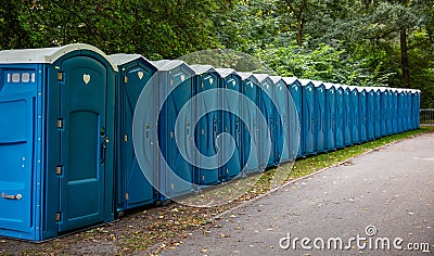 Portable WC cabins in the park. A line of chemical toilets for a festival, against a forest Stock Photo