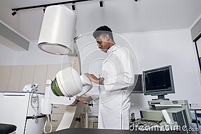 Portait of handsome young confident focused African man doctor, wearing white uniform, working in modern clinic with Stock Photo