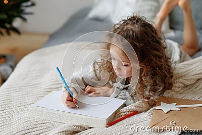 Portait of small lovely beautiful curly child draws pictures on blank white sheet of paper, wants to congratulate her Stock Photo