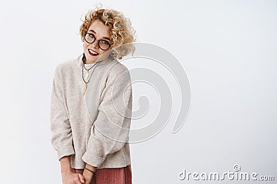 Portarit of cute and shy flirty blond girl in glasses and sweater making lovely gazes at camera smiling sensually and Stock Photo