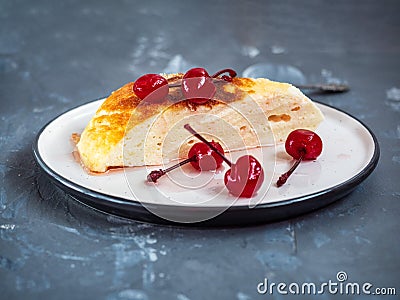 Portion of cottage cheese casserole on a ceramic saucer with decorated canned cherries, several vishinok fell on a saucer, shot Stock Photo