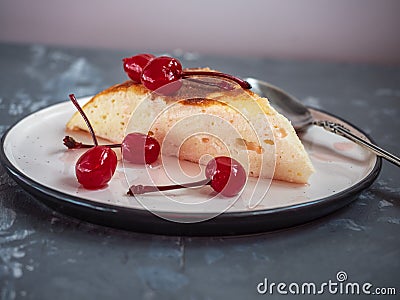 Portion of cottage cheese casserole on a ceramic saucer with a teaspoon, casserole decorated with canned cherries Stock Photo