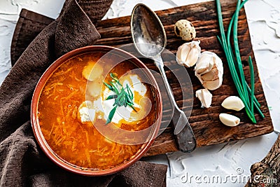 A portion of red borscht in a brown plate, next to an old wooden Board garlic and quail egg, green leeks and driftwood. White sour Stock Photo