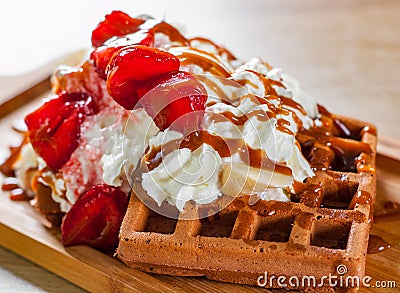 Portion of Viennese waffle with cream, strawberry, banana, caramel and ice cream on wooden table Stock Photo