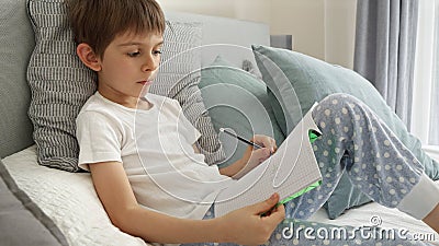 Portrai of little boyworking on his homework in bed, writing in a notebook with concentration. Importance of education and child Stock Photo