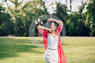 Portrait of active brunette girl in bandana posing in summer park. She wears white clothes, long pink shirt. She is Stock Photo