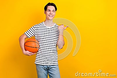 Portrait of active guy wear stylish t-shirt hold bascketball ball look directing at sale empty space isolated on yellow Stock Photo