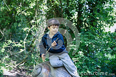 Portrait active kid sitting on a wooden statue at public park,Happy child wearing blue jacket playing outdoor in Spring forest, Stock Photo