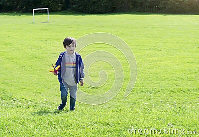 Portrait active little boy playing with toy airplane against green nature background, Child throwing foam airplane in green field Stock Photo