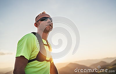 Portrait of Active mountain trail runner dressed bright t-shirt with backpack and sport sunglasses resting while he sky running by Stock Photo