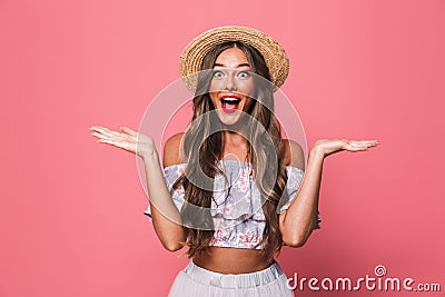 Portrait of adorable glamour woman 20s wearing straw hat screaming and throwing arms aside, isolated over pink background in stud Stock Photo