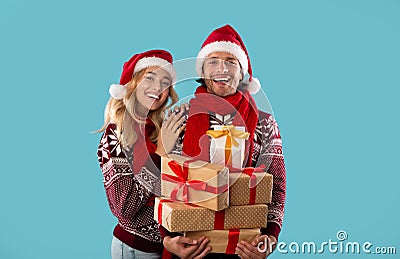 Portrait of adorable young couple in Christmas outfits holding heap of gift boxes on blue background Stock Photo