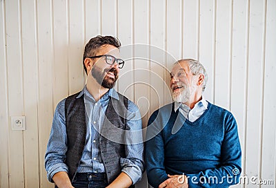 A portrait of adult hipster son and senior father sitting on floor indoors at home. Stock Photo