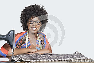 Portrait of an African American female fashion designer with sewing machine and cloth over gray background Stock Photo