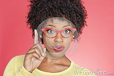 Portrait of an African American woman in retro glasses pointing upward over colored background Stock Photo