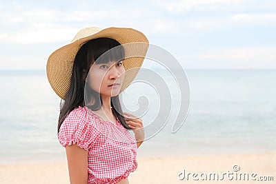 Portrait alone woman standing at coast with hat on blur blue sea and blue sky. Stock Photo