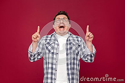 Portrait of amazed funny middle aged man in checkered shirt, eyeglasses standing, looking up, shocked face and pointing at up Stock Photo