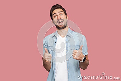 Portrait of amazed handsome bearded young man in blue casual style shirt standing, thumbs up and looking at camera with surprised Stock Photo