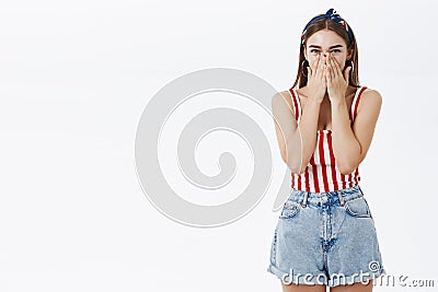 Portrait of amused popular pinup euroepan woman in striped top and denim shorts chuckling covering mouth with palms not Stock Photo