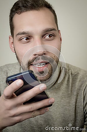 Portrait of an amused young man who is recording an audio message on his smartphone Stock Photo
