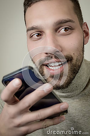 Portrait of an amused young man who is recording an audio message on his smartphone Stock Photo