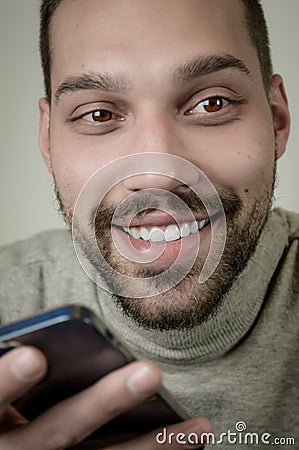 Portrait of an amused young man who is recording an audio message on his smartphone Stock Photo