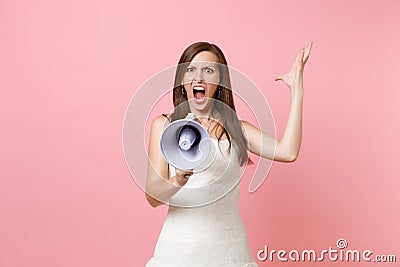 Portrait of angry irritated bride woman in wedding dress screaming in megaphone and spreading hands on pink Stock Photo